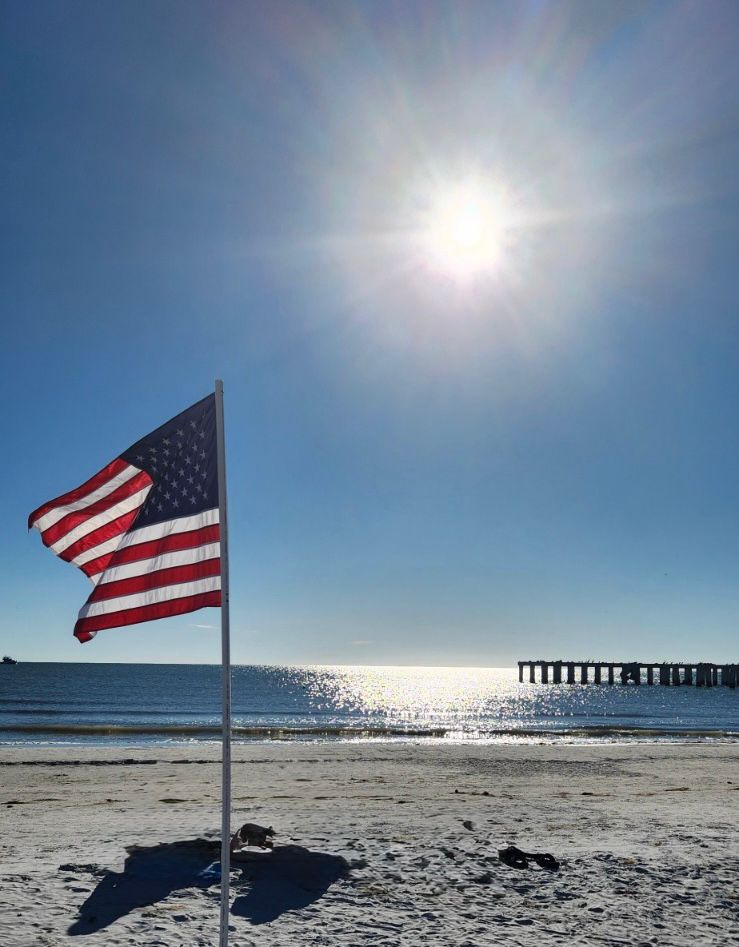 American flag on Fort Myers Beach with Gulf of Mexico and historic pier in Southwest Florida